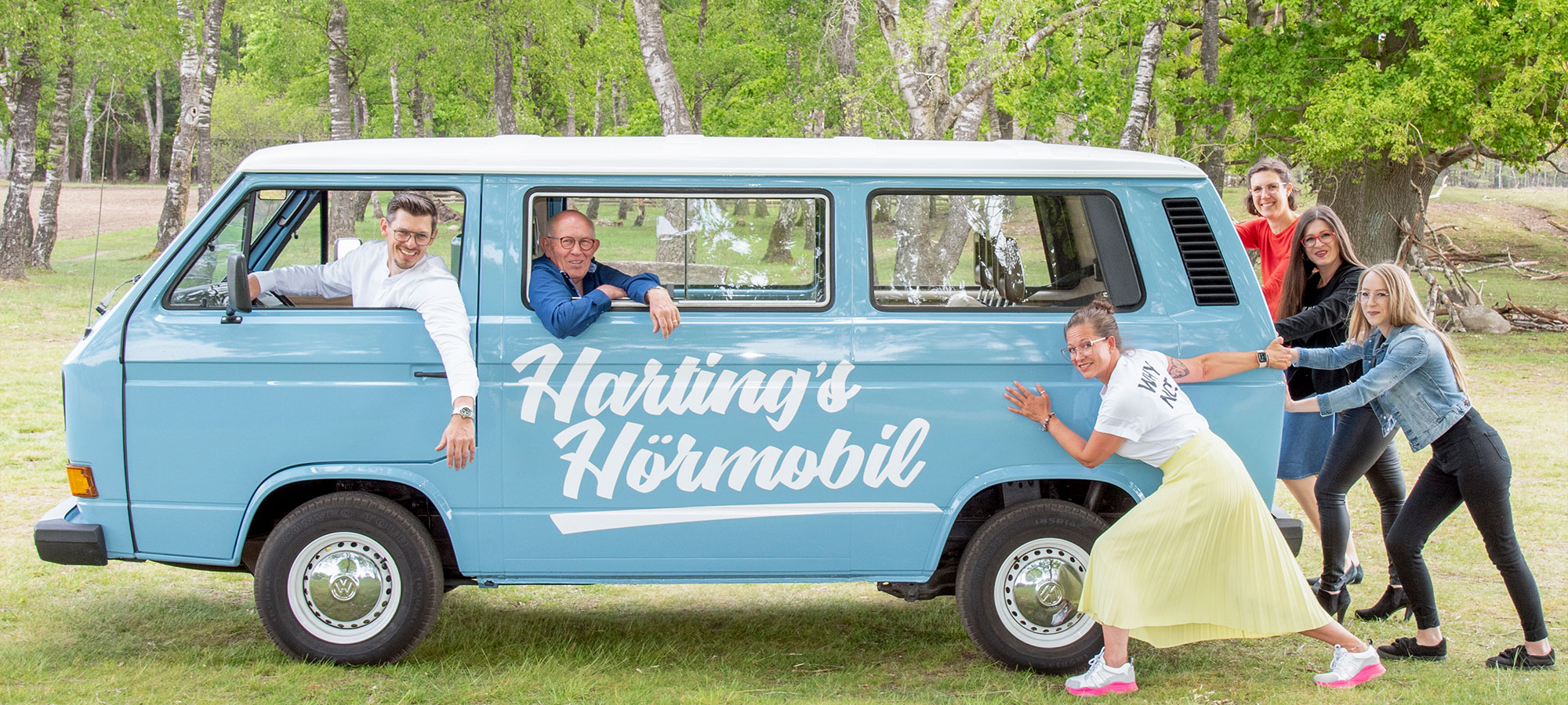 Gruppenfoto vom Harting Team mit einem blauen Van. Aufschrift auf dem Van: "Harting's Hörmobil"