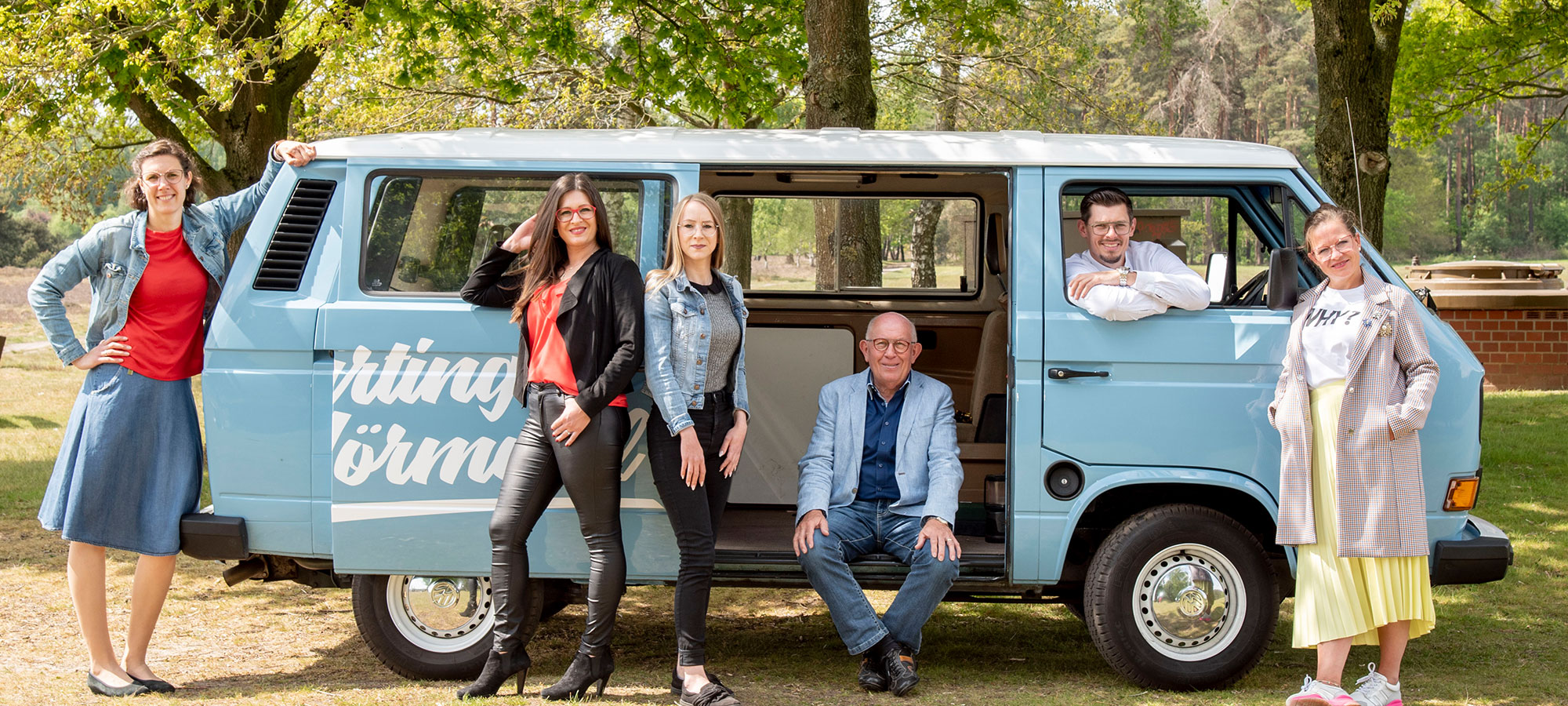 Gruppenfoto vom Harting Team mit einem blauen Van. Aufschrift auf dem Van: "Harting's Hörmobil"