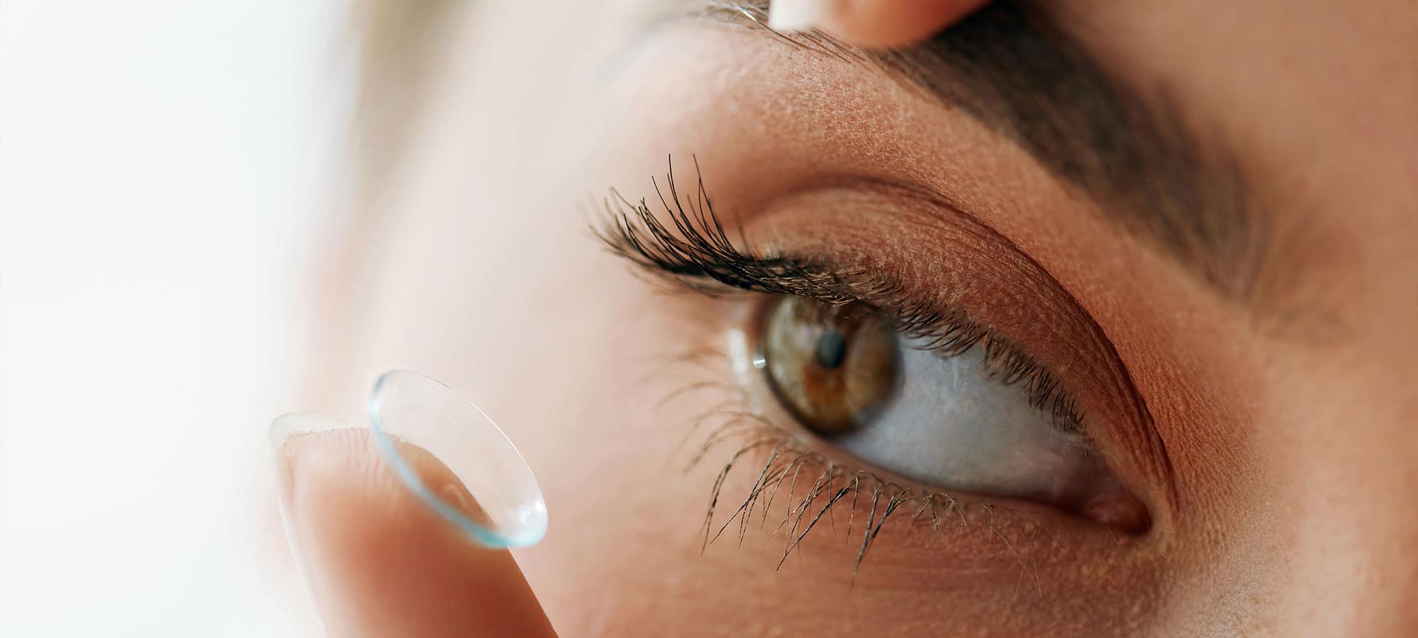 Nahaufnahme vom Auge einer Frau, welche eine Kontaktlinse auf Ihrem Finger hat